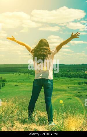 Giovane donna in piedi in un campo di grano con alba sullo sfondo. Una vista dal retro di una donna in piedi su una montagna e ammira la bella Foto Stock