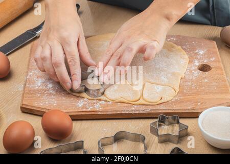 Cottura, taglio di biscotti fatti in casa utilizzando una forma a cuore metallico. Le mani delle donne. Primo piano Foto Stock