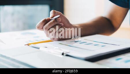 Primo piano contabile mano tenendo penna lavorare su dati di finanza aziendale, documento contabile e computer portatile in ufficio, business concept. Foto Stock