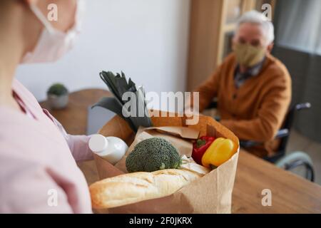 Primo piano di una giovane donna che porta generi alimentari a un uomo anziano in sedia a rotelle, concetto di servizio di consegna di cibo, spazio di copia Foto Stock