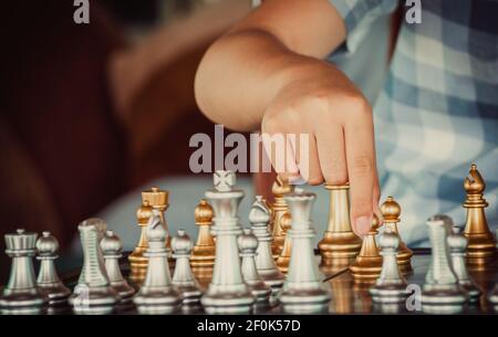 Primo piano di un ragazzo sicuro di mano che sposta gli scacchi della pedina d'oro allo sviluppo nel gioco di successo della concorrenza quale nuovo piano di strategia, leader e concetto di lavoro di squadra. Foto Stock