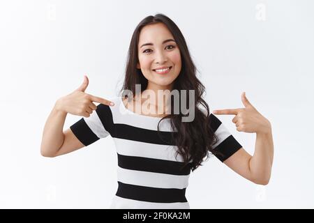 Spensierato, uscente buona-guardare donna asiatica in t-shirt a righe che si indica come proporre la propria candidatura, parlando realizzazioni personali, vantare o. Foto Stock