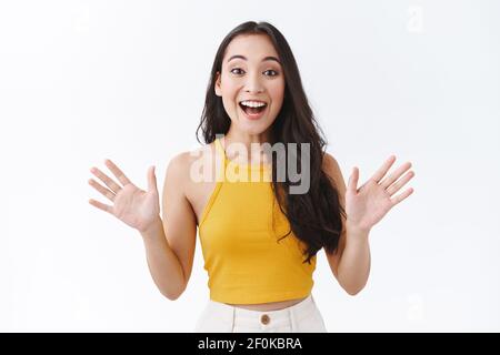 Felice, affascinato bella-look moderna donna asiatica in giallo top, alzano le mani lateralmente e sorridendo come emotivamente raccontare le notizie sorprendenti Foto Stock