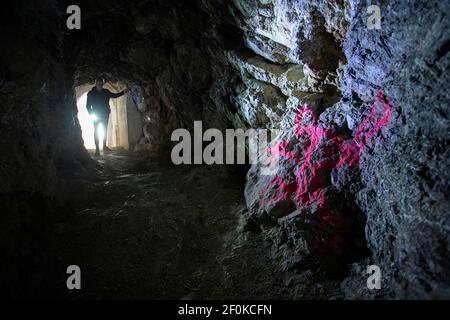 Uomo con una torcia in piedi nello storico sistema sotterraneo italiano a Unska Kolisevka, illuminando il cartello di pericolo sulle pareti, Slovenia Foto Stock