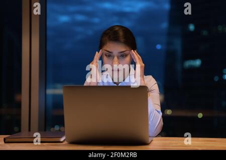 Primo piano su ha sottolineato indiane businesswoman che toccano i templi, lavorando di notte Foto Stock