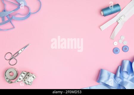 Accessori per cucire su fondo rosa con aghi, rocchetto di filo, forbici e metro a nastro Foto Stock