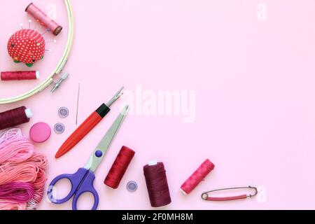 Composizione con accessori da cucire su fondo rosa con aghi, un rocchetto di filo, forbici e un nastro di misurazione Foto Stock