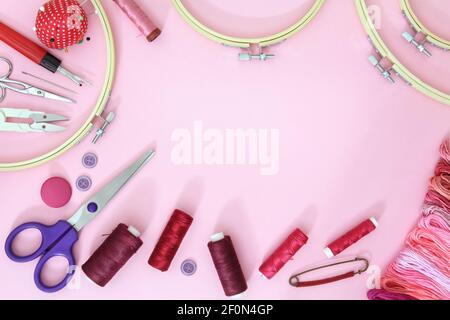 Accessori per cucire su fondo rosa con aghi, rocchetto di filo, forbici e metro a nastro Foto Stock