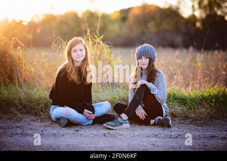 Due belle ragazze di Tween che si siedono all'aperto in autunno, retroilluminate. Foto Stock