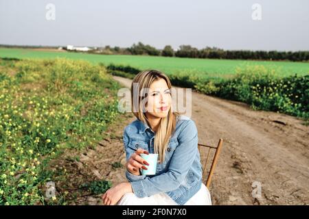 giovane donna che gusta il caffè in campagna seduto su un sedia Foto Stock