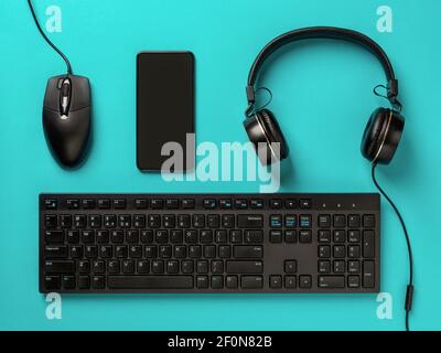 Cuffie, smartphone, mouse per pc e tastiera per computer desktop su sfondo turchese. Dispositivi e gadget moderni. Business online, apprendimento. Foto Stock