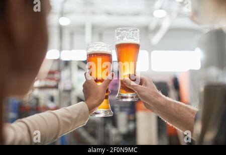 Primo piano di due lavoratori che tengono bicchieri da birra mentre ispezionano la qualità della produzione e la filtrazione presso la fabbrica di birra, copisteria Foto Stock