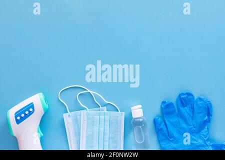 Concetto di protezione da virus corona piatto. Termometro a infrarossi senza contatto per il corpo, guanti in lattice, maschere monouso e disinfettante su sfondo blu con Foto Stock