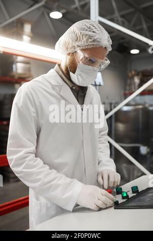 Verticale del lavoratore maschile premendo i pulsanti sul pannello di controllo durante il funzionamento delle unità della macchina in un impianto chimico Foto Stock