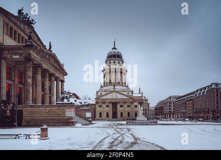 Vista panoramica sulla neve e sull'inverno della famosa piazza Gendarmenmarkt con la sala concerti di Berlino e la cattedrale tedesca. Luce del mattino presto con nuvole dopo Foto Stock