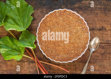 Tradizionale torta di rabarbaro su una tavola rustica di legno con gambo di rabarbaro. La torta è composta da un toffee toping fatto di avena arrotolata, panna, sciroppo, zucchero, farina Foto Stock