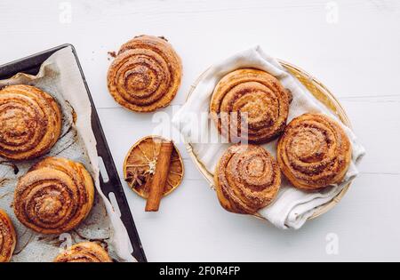 Panini alla cannella fatti in casa appena sfornati in cestino e su una teglia da forno al mattino all'interno, concetto di colazione. Vista dall'alto. Foto Stock