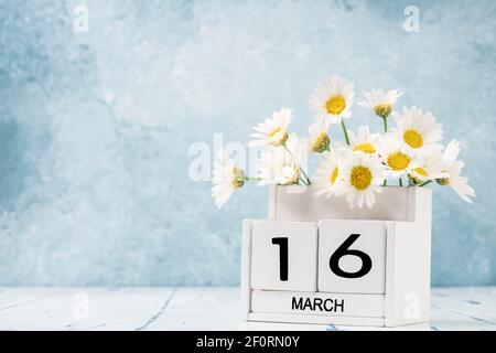 Calendario cubo bianco per marzo decorato con fiori margherita sopra sfondo blu con spazio per la copia Foto Stock