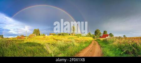 Arcobaleno sopra il cielo tempestoso. Paesaggio rurale con arcobaleno su cielo scuro tempestoso in campagna in estate sera. Foto Stock