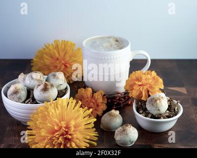 Palle di torta al cappuccino, tartufo aromatizzato al caffè come dessert, decorato con fiori d'arancio autunnali su un tavolo di legno con tazza di caffè e bo in ceramica bianca Foto Stock