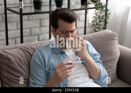 L'uomo millenario si sente male strofinare il naso vedere la febbre sul termometro Foto Stock