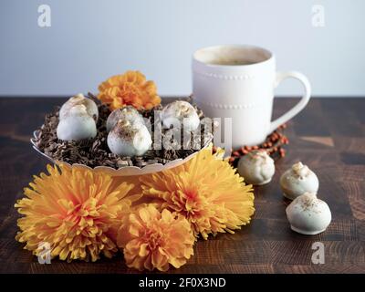 Palle di torta al cappuccino, tartufo aromatizzato al caffè come dessert, decorato con fiori d'arancio autunnali su un tavolo di legno con tazza di caffè e bo in ceramica bianca Foto Stock