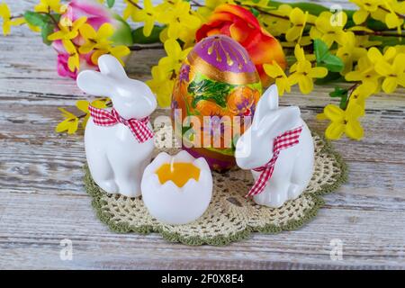 Coniglietti di Pasqua, uova di Pasqua e una candela a forma di uovo con un bouquet di fiori sullo sfondo su un tavolo di legno. Foto Stock