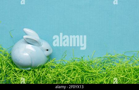 Coniglietto pasquale bordo di un coniglietto di ceramica blu e grattugiato erba di carta su fondo di tessuto blu Foto Stock