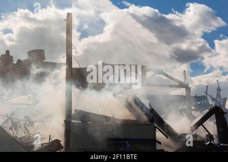 Disastro tecnologico, incendio, edifici industriali distrutti, fumo e spruzzi d'acqua Foto Stock