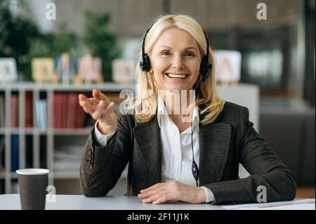 Webcam ritratto di una donna matura di successo amichevole. Una donna d'affari sicura in una cuffia comunica con i colleghi tramite una videoconferenza, gesti con le mani, guarda la fotocamera con un sorriso. Foto Stock