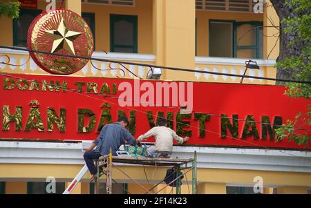 Lavoratori che puliscono il cartello sulla parte anteriore di un edificio dell'Esercito popolare del Vietnam (Qu‰n ??i NH‰n d‰n vi?t Nam) edificio, Distretto 1, ho Chi Minh Cit Foto Stock