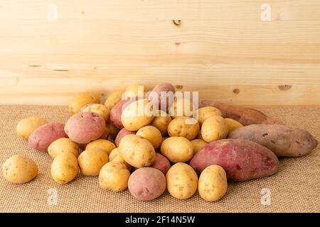 Patate gialle organiche crude, patate rosse e patate rosse dolci si avvicinano su sfondo rustico con spazio copia Foto Stock