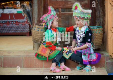 Due Fiore Hmong ragazze con copricapo seduto su un gradino indossando abiti indigeni della tribù delle colline della provincia di Lao Cai, Vietnam. Sapa Foto Stock