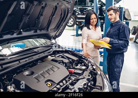 Scena del centro di assistenza auto. Il meccanico comunica con il cliente Foto Stock