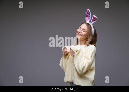 giovane donna, bionda, con orecchie bianche e un maglione leggero su sfondo grigio Foto Stock