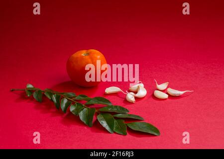 Spicchi d'aglio con foglie di curry e pomodoro, arrangiati splendidamente su uno sfondo rosso testurizzato, isolati. Foto Stock