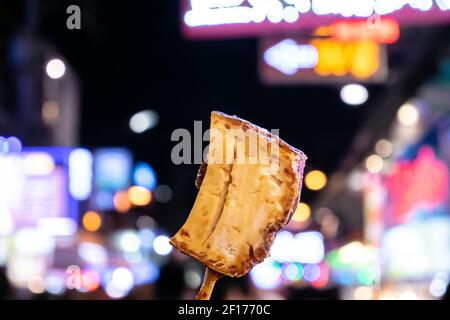 Tofu fritto e stinky, un primo piano della cucina taiwanese di cagliata di fagioli fritti su sfondo colorato e sfocato bokeh vita notturna nel cibo di strada a Taiwan notte m. Foto Stock