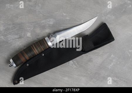 Un elegante coltello da caccia con scabarda e manico in pelle su fondo grigio cemento. Messa a fuoco selettiva. Foto Stock