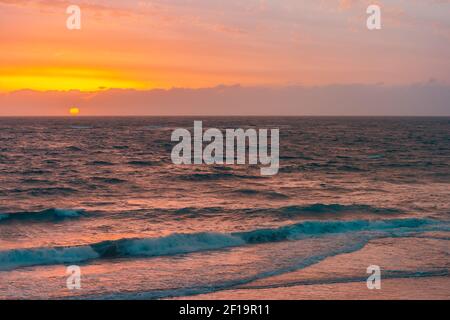 Grande sole giallo che cade dietro il mare a Christies Beach durante il tramonto, Australia del Sud Foto Stock