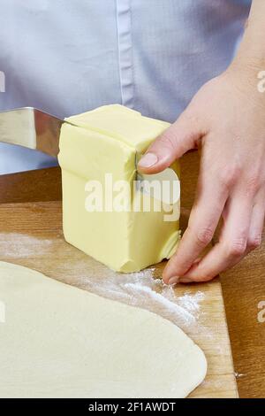 Lo chef taglia un grosso pezzo di burro spalmato sul preparazione dell'impasto cheesecakes serie ricette complete di cucina alimentare Foto Stock