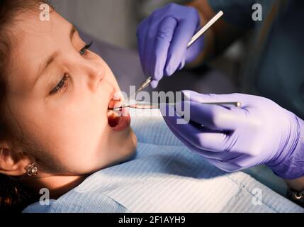 Primo piano di paziente ragazza con bocca aperta mentre dentista controllare i denti del bambino. Stomatologo che esamina i denti del bambino con l'esploratore dentale e lo specchio. Concetto di odontoiatria pediatrica e cura dentale. Foto Stock