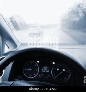 Vista dall'interno del veicolo - conducente con volante e cruscotto. Inverno maltempo piovoso e guida pericolosa su strada. Foto Stock