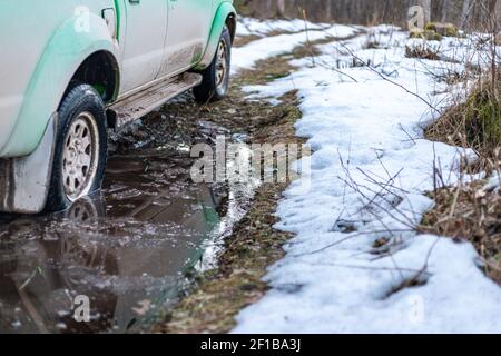 auto verde in grande puddle su strada sterrata nella foresta Foto Stock