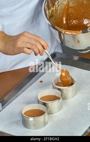 Il cuoco versa l'impasto in forme per preparare i cupcake Foto Stock