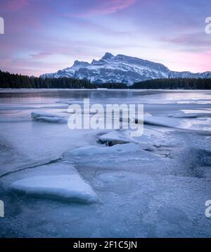 Tramonto colorato sul lago ghiacciato con montagna isolata sullo sfondo, girato durante il tramonto al Two Jack Lake, Banff National Park, Alberta, Canada Foto Stock