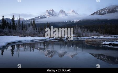 Foto invernale pre-alba delle Montagne Rocciose canadesi con montagna riflessa in acqua, sparata a Three Sisters Mountain, Canmore, Alberta, Canada Foto Stock