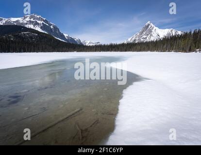 Mezzo lago alpino ghiacciato circondato da montagne innevate, sparato al lago di Watridge, Kananaskis, Alberta, Canada Foto Stock