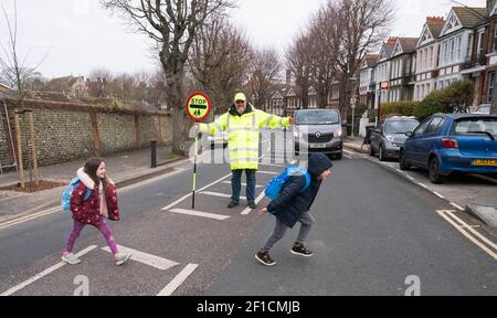 Brighton UK 8 marzo 2021 - l'uomo Lollipop Simon Moss dà il benvenuto ai bambini alla scuola elementare di St Luke a Brighton questa mattina, mentre le restrizioni di blocco del governo in Inghilterra stanno cominciando ad essere attenuate . Le scuole e le università stanno riaprendosi a tutti gli allievi oggi in tutta l'Inghilterra: Credit Simon Dack / Alamy Live News Foto Stock