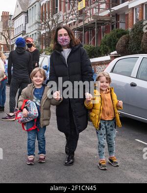 Brighton UK 8 marzo 2021 - i gemelli felici ed i loro genitori della madre arrivano alla scuola primaria del St Luke a Brighton questa mattina come le restrizioni di blocco di governo in Inghilterra stanno cominciando ad essere attenuate. Le scuole e le università stanno riaprendosi a tutti gli allievi oggi in tutta l'Inghilterra: Credit Simon Dack / Alamy Live News Foto Stock