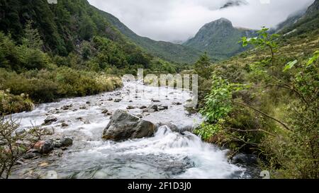 Fiume che scorre attraverso la valle, circondato da montagne avvolte nelle nuvole, girato al Nelson Lakes National Park, Nuova Zelanda Foto Stock